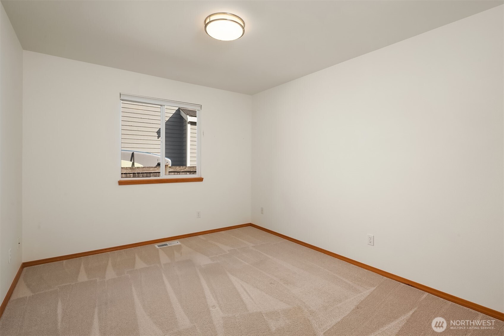 Empty carpeted bedroom with a window and flush-mount ceiling light.