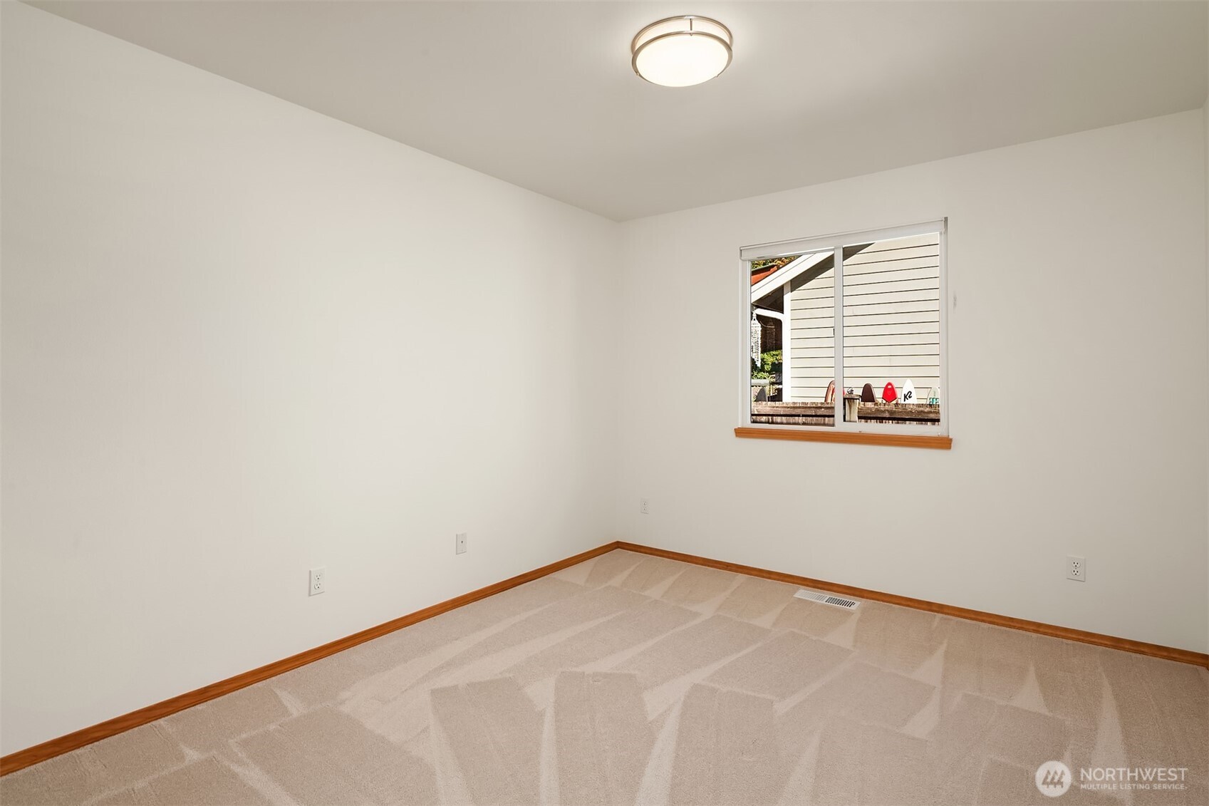 Empty carpeted room with white walls, wood trim, and a window.