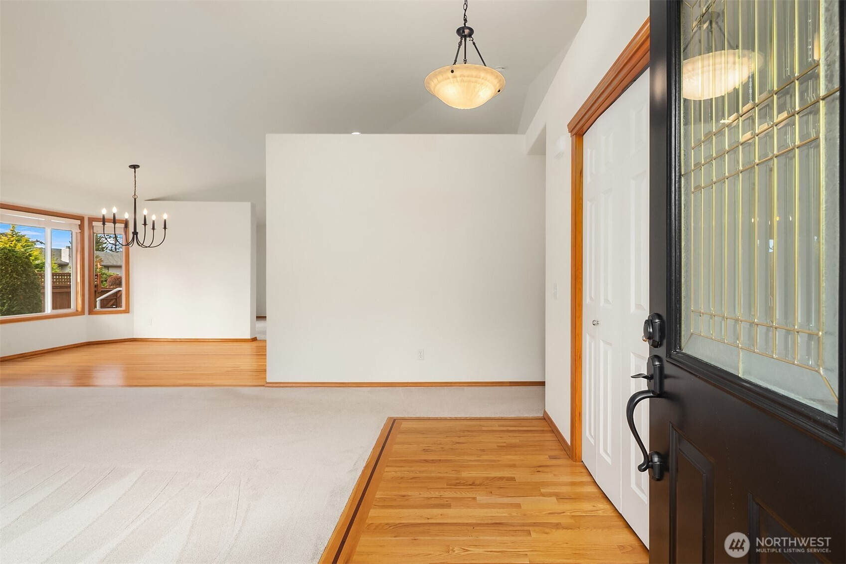 Entryway with a decorative glass front door, hardwood flooring, and a carpeted adjoining room.