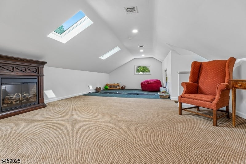 Finished attic room with skylights, beige carpet, a fireplace, and an orange wingback chair.