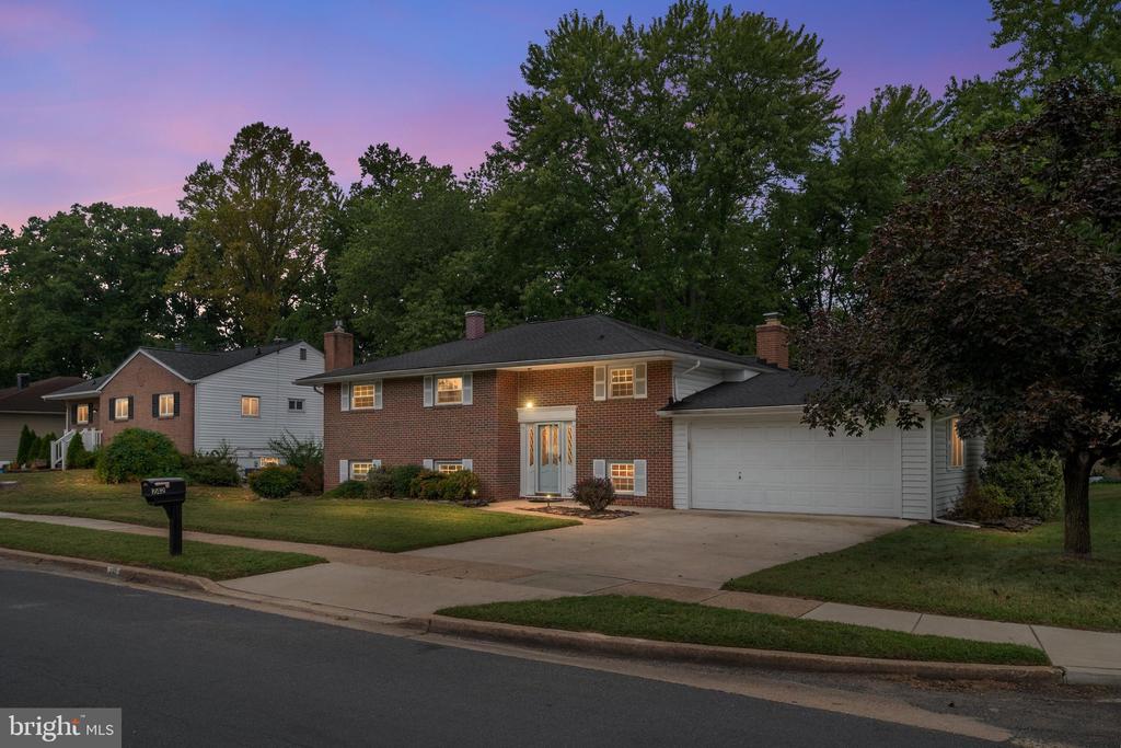 Brick-and-siding home at dusk with an attached garage, wide driveway, and mature trees.