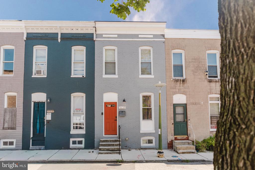 Gray brick rowhouse with a bright orange front door on a city street.