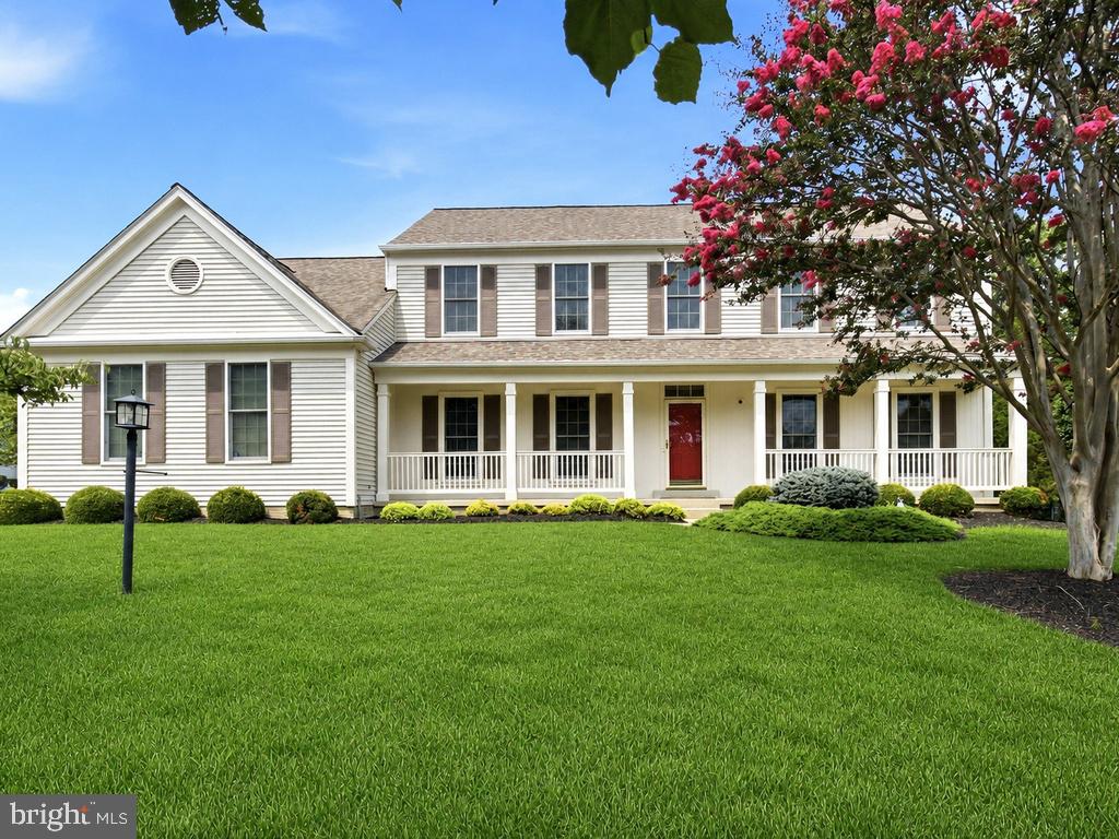 White two-story home with a red front door, covered porch, and pink flowering tree.