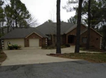 Brick house with an attached garage and broad curved driveway beneath mature trees.
