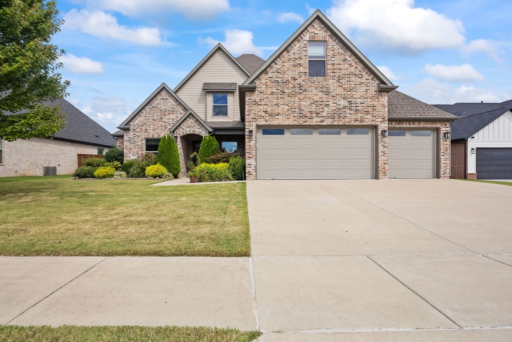 Brick-front home with a three-car garage, landscaped lawn, and broad driveway.