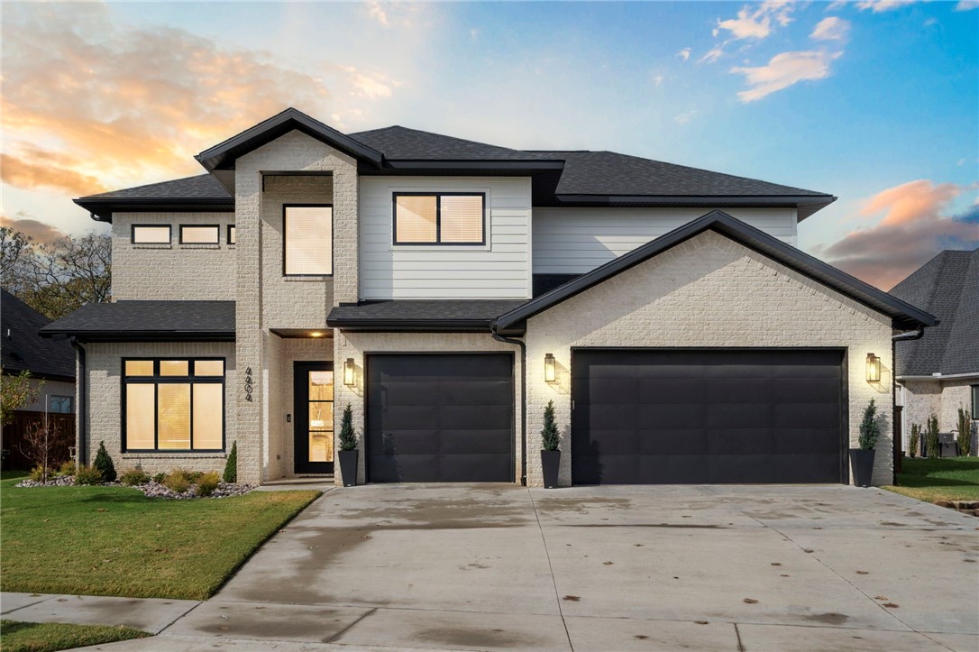 Two-story modern home with light stone siding, a dark roof, and a three-car garage.