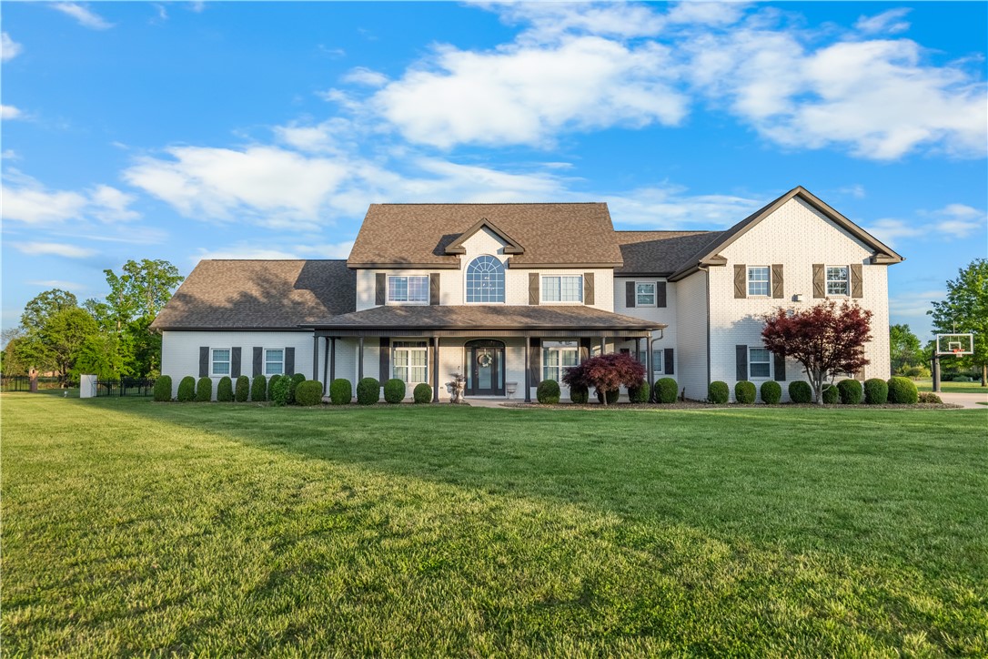 Large two-story house with a covered porch, landscaped shrubs, and a broad green lawn.