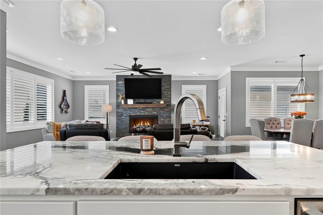 Kitchen island with marble countertop overlooks a living room with a stone fireplace and television.