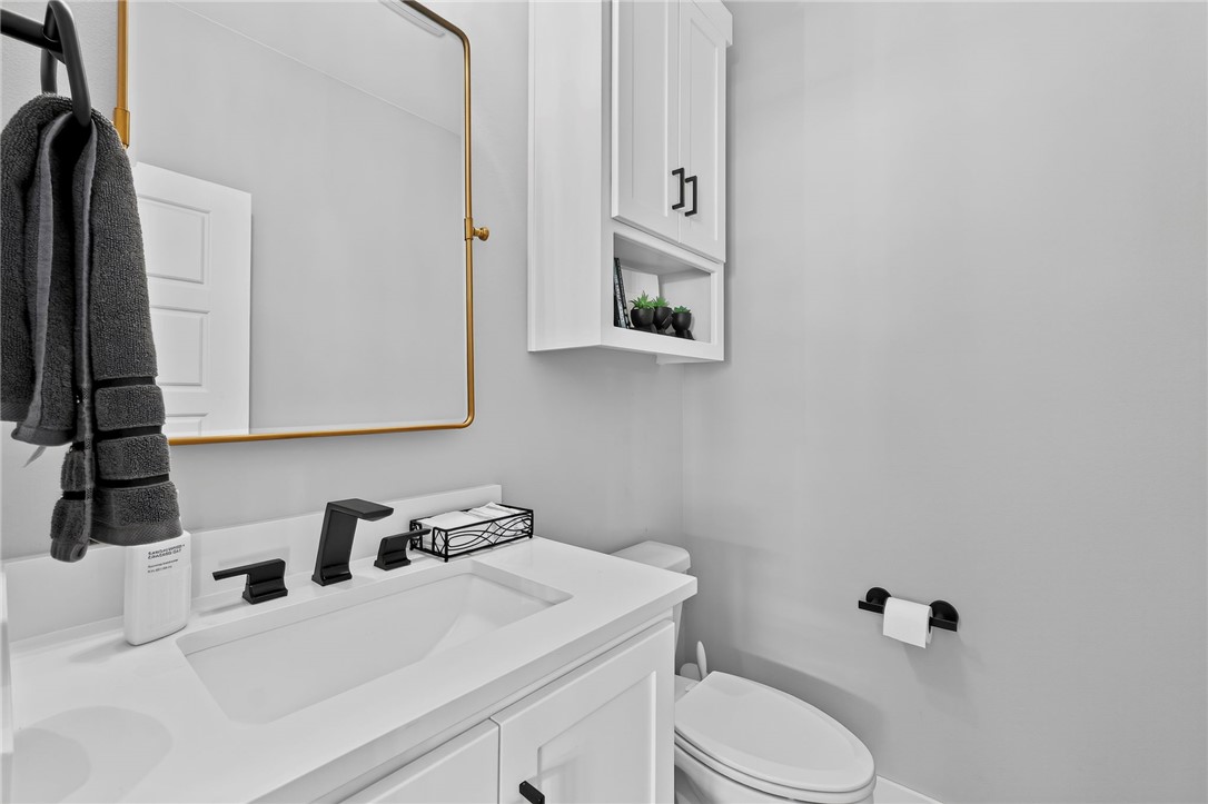Bathroom vanity with a black faucet, gold-framed mirror, wall cabinet, and toilet.