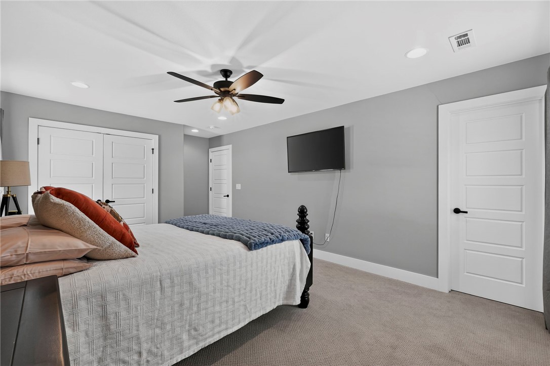 Furnished bedroom with a ceiling fan, wall-mounted television, and white paneled doors.