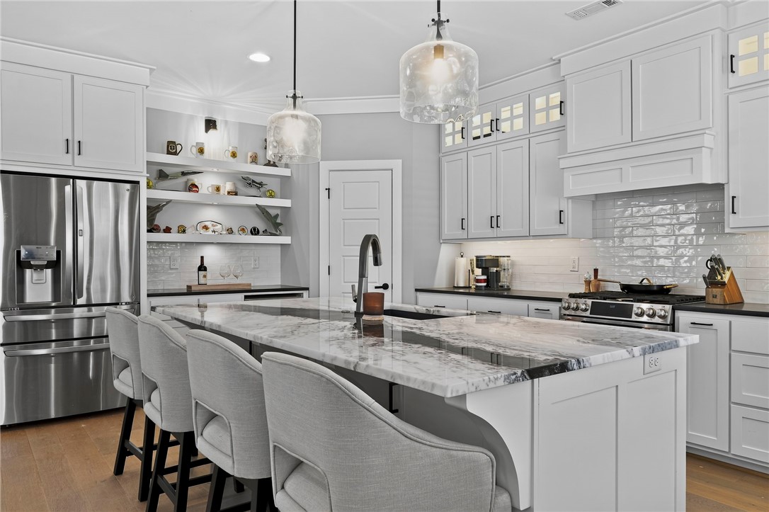 Bright white kitchen with a large marble island, gray bar stools, and stainless steel appliances.