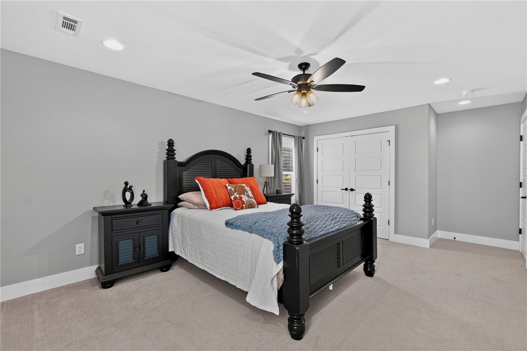 Furnished bedroom with a black carved bed, blue throw, orange pillows, and ceiling fan.