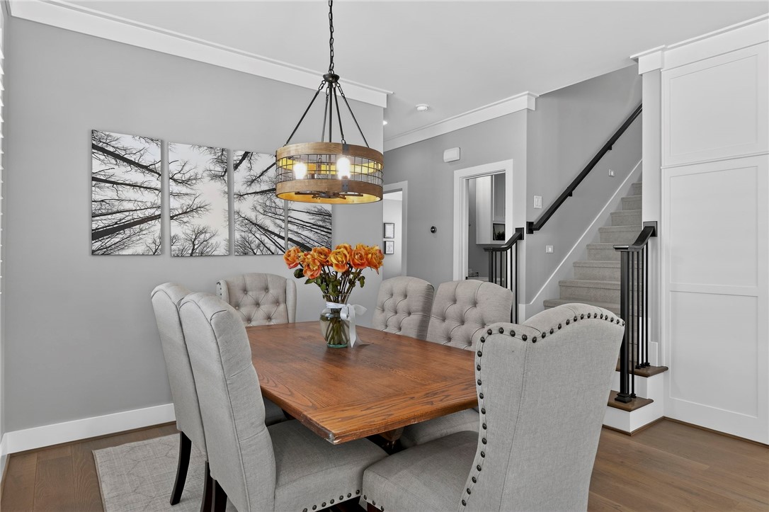 Dining room with a wood table, gray upholstered chairs, orange flowers, and a staircase.