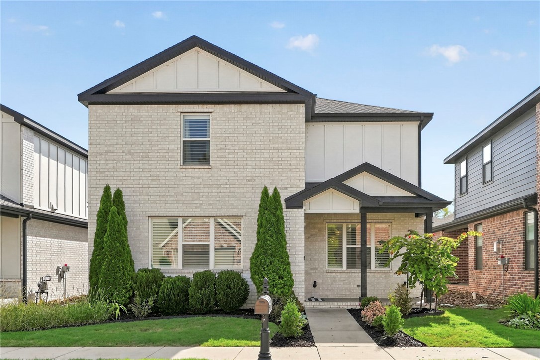 Two-story light brick house with a covered entry, landscaped lawn, and front walkway.