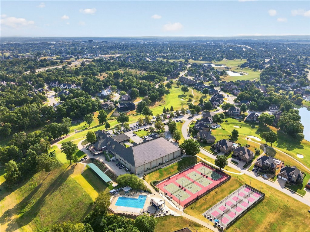 Aerial view of a golf-course neighborhood with tennis courts, a swimming pool, and homes.