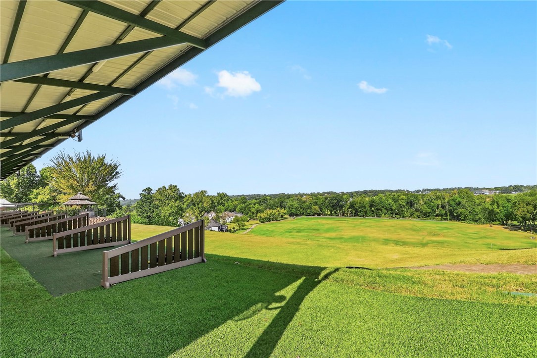Covered patio with turf seating overlooks a broad green field and tree-lined horizon.
