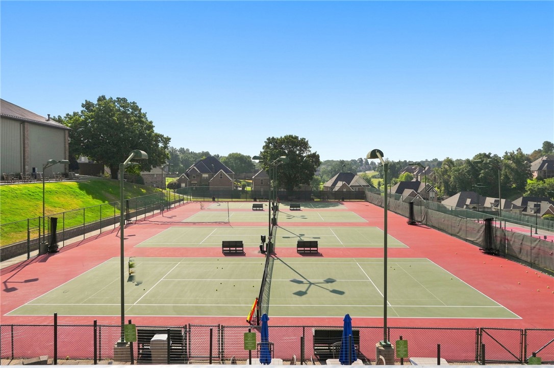 Fenced tennis courts with benches and neighborhood homes in the background.