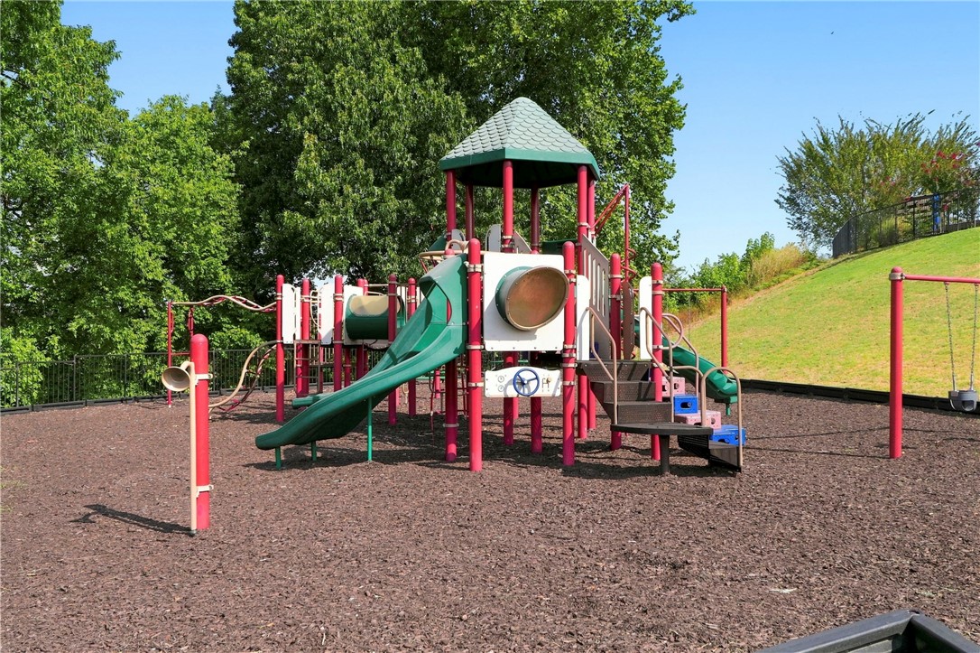 Outdoor playground with colorful slides and climbing structures beneath leafy trees.