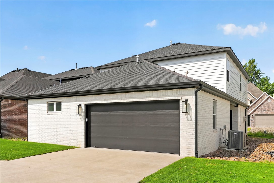 Two-story home with white brick exterior, dark double garage door, and wide concrete driveway.