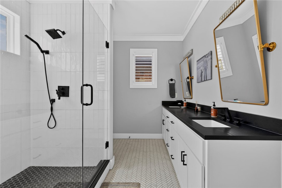 Modern bathroom with a glass shower, black fixtures, and a long white vanity with a black countertop.