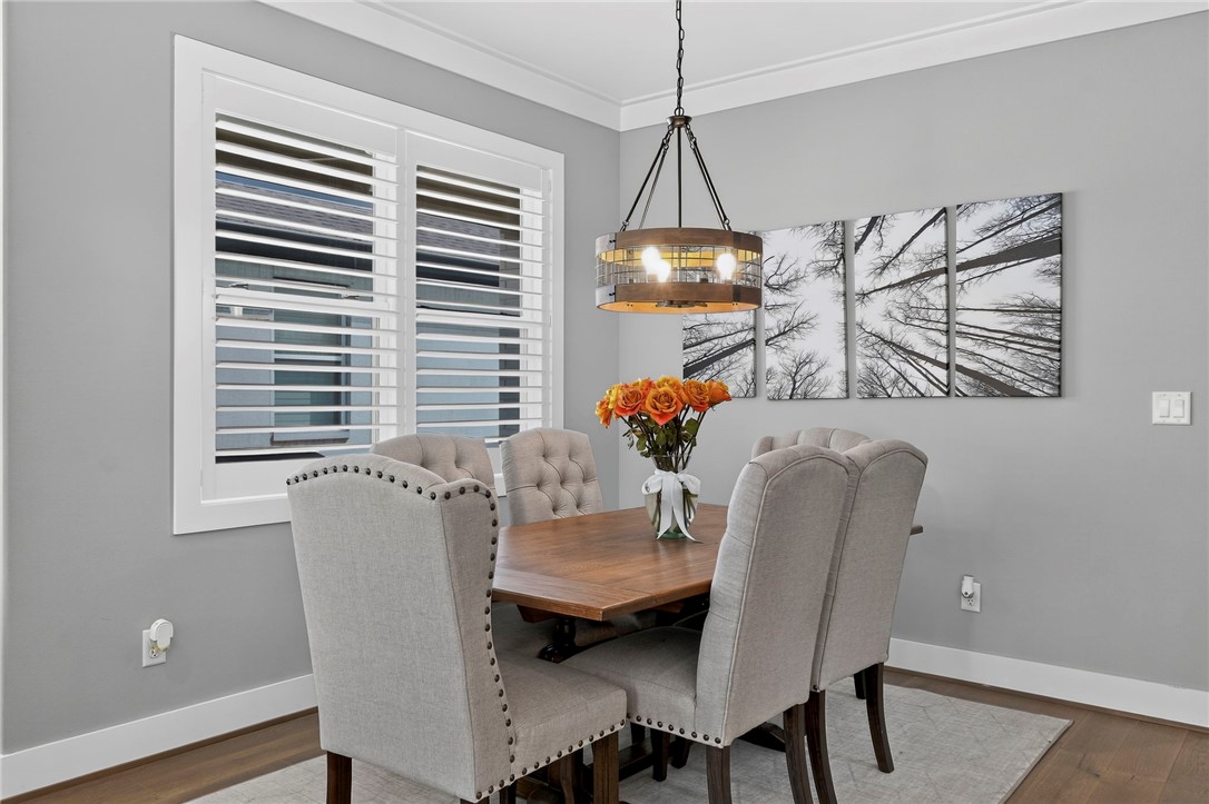 Dining room with a wood table, upholstered chairs, plantation shutters, and a pendant light.
