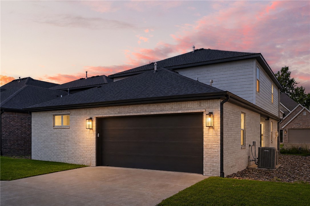 House exterior with a wide garage and concrete driveway beneath a pink sunset sky.