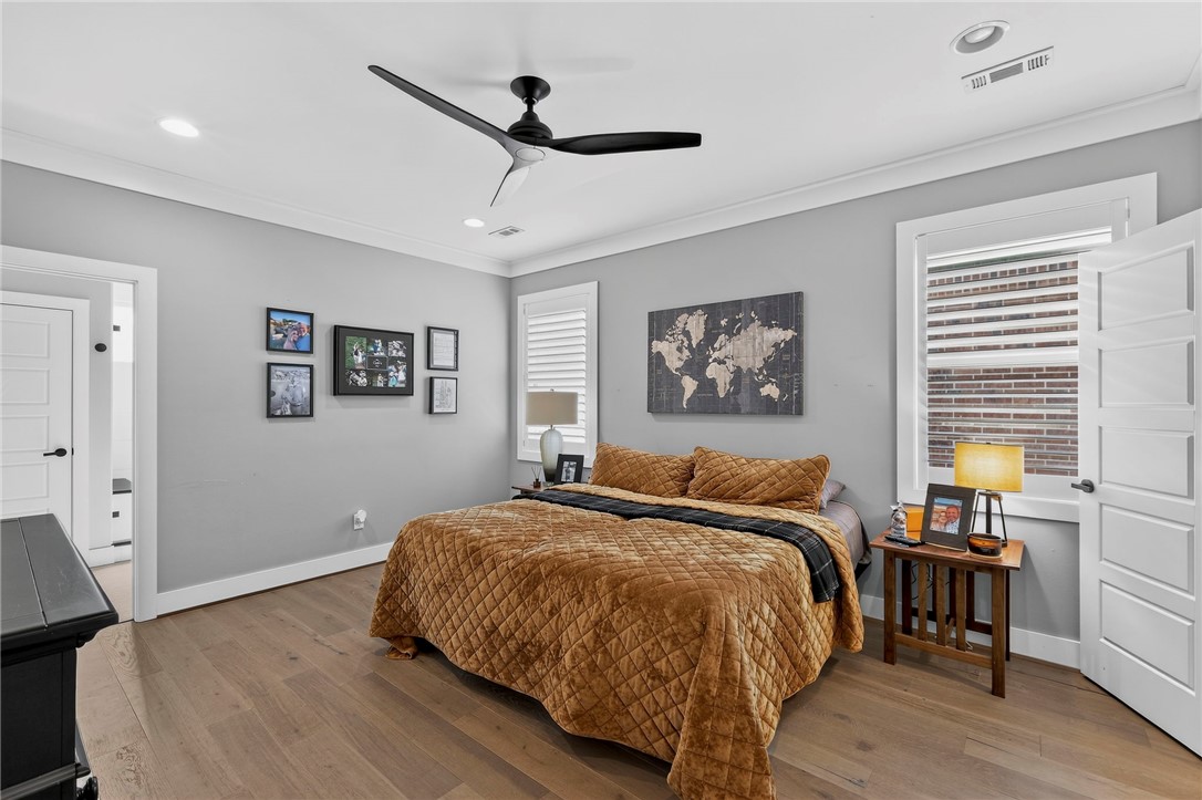 Bedroom with a brown quilted bedspread, black ceiling fan, framed art, and light wood flooring.