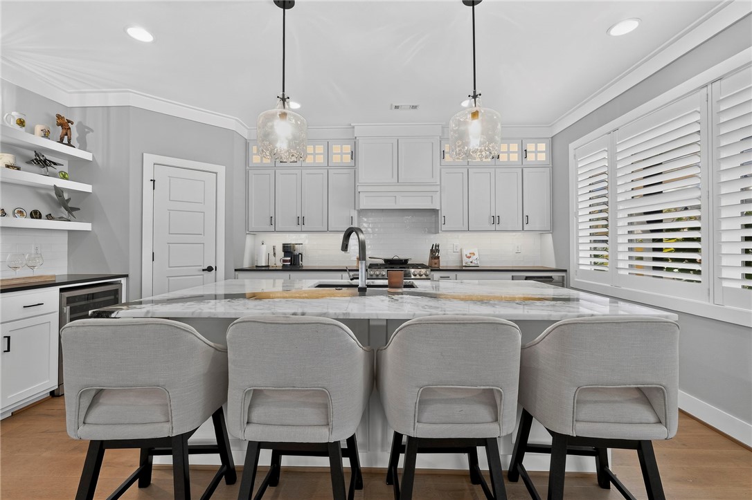 Kitchen with a marble island, four upholstered stools, white cabinets, and plantation shutters.