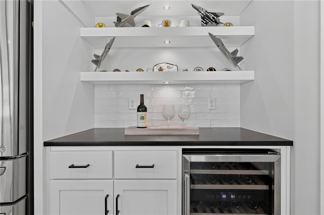 Built-in wet bar with a wine refrigerator, white tile backsplash, and model airplanes on display shelves.