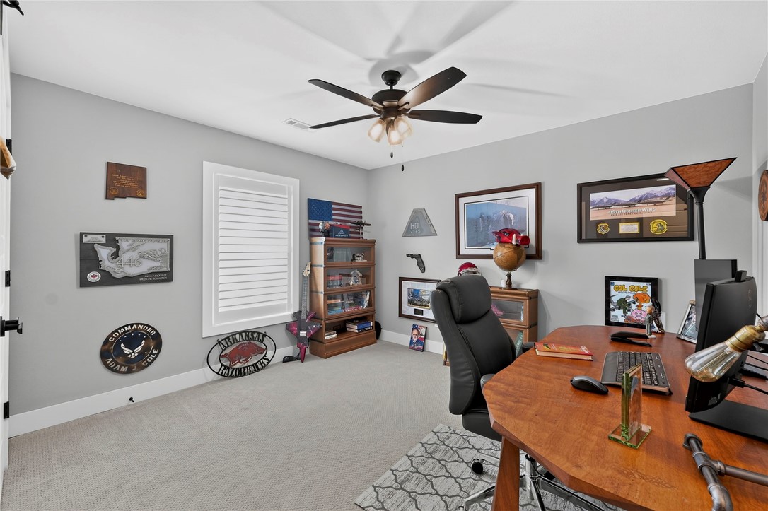 Furnished home office with a wooden desk, black chair, ceiling fan, and sports memorabilia.