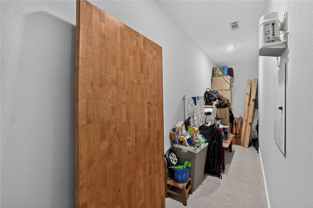 Narrow carpeted storage area crowded with bins, luggage, and leaning boards.