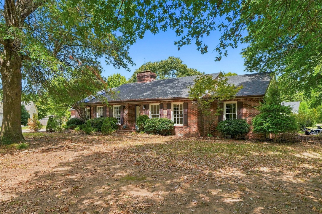 Single-story brick house with white shutters, mature trees, and a broad front yard.