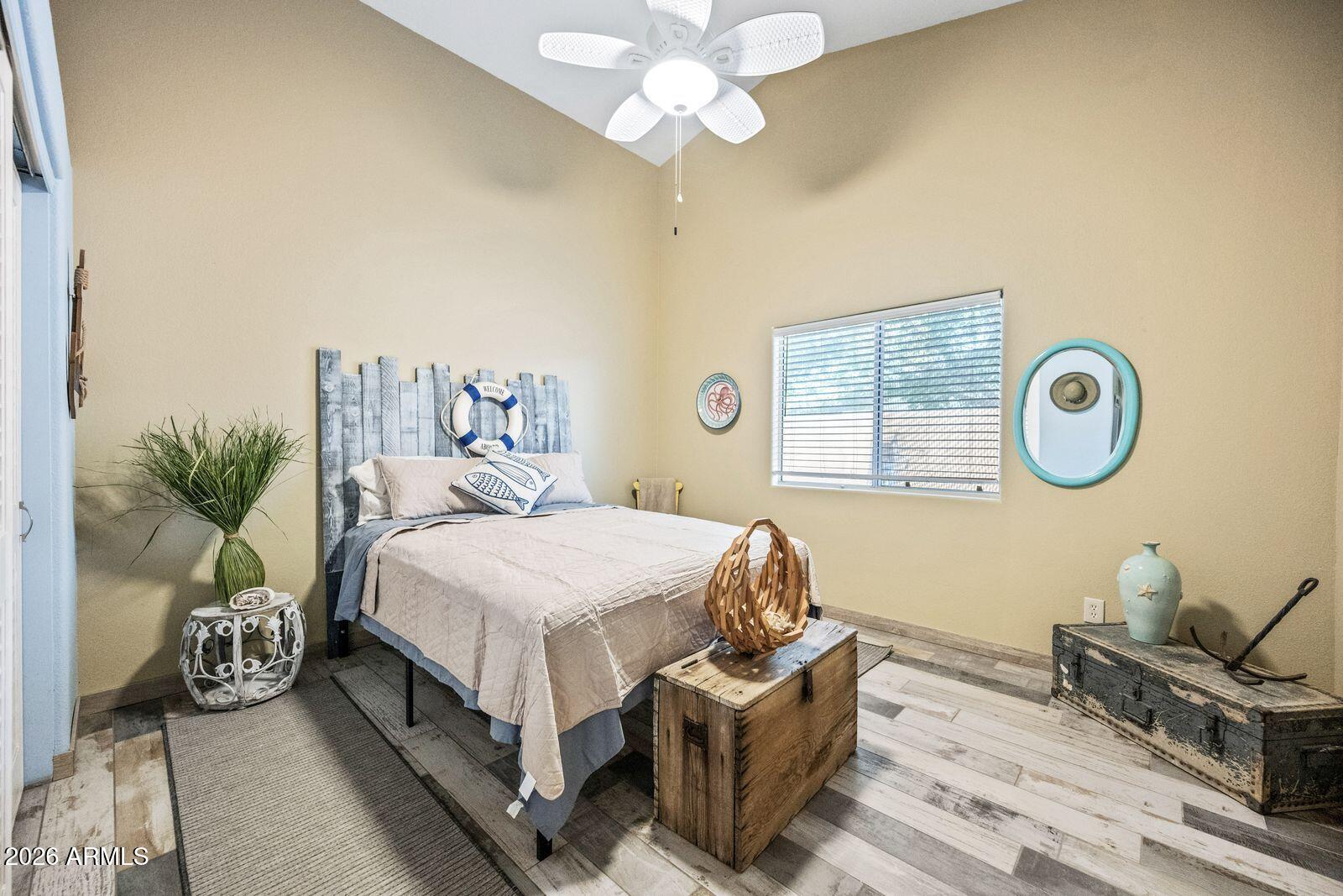 Furnished bedroom with nautical decor, a pale bed, white ceiling fan, and wooden chest.