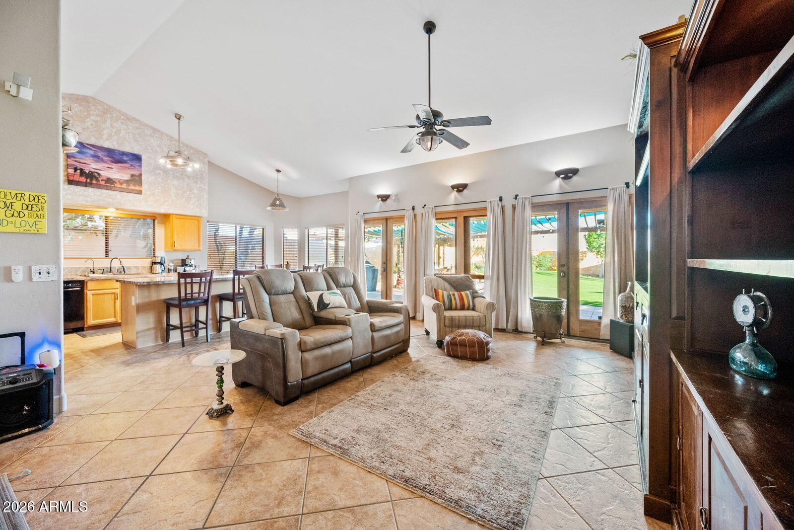 Living room with vaulted ceiling, tiled floors, and sliding glass doors overlooking the backyard.