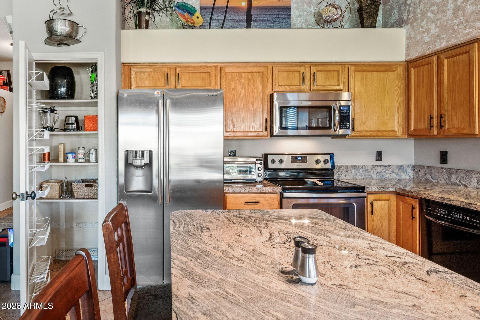 Kitchen with granite island, honey-toned cabinets, stainless appliances, and an open pantry.