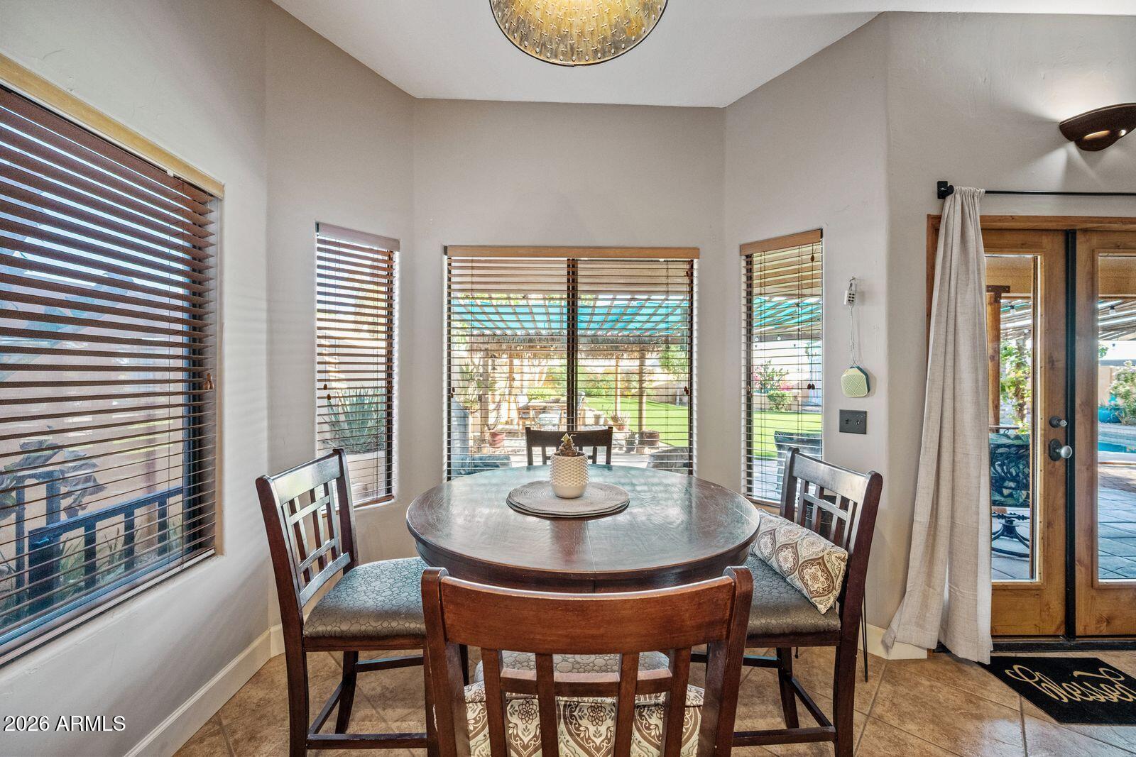 Dining area with a round wooden table, tall windows, and a view of the covered patio and yard.