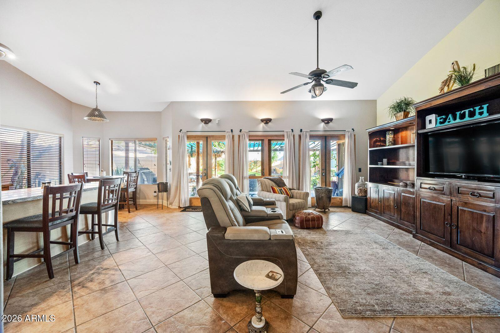 Open-plan living and dining room with recliners, tiled floors, and glass doors to the backyard.
