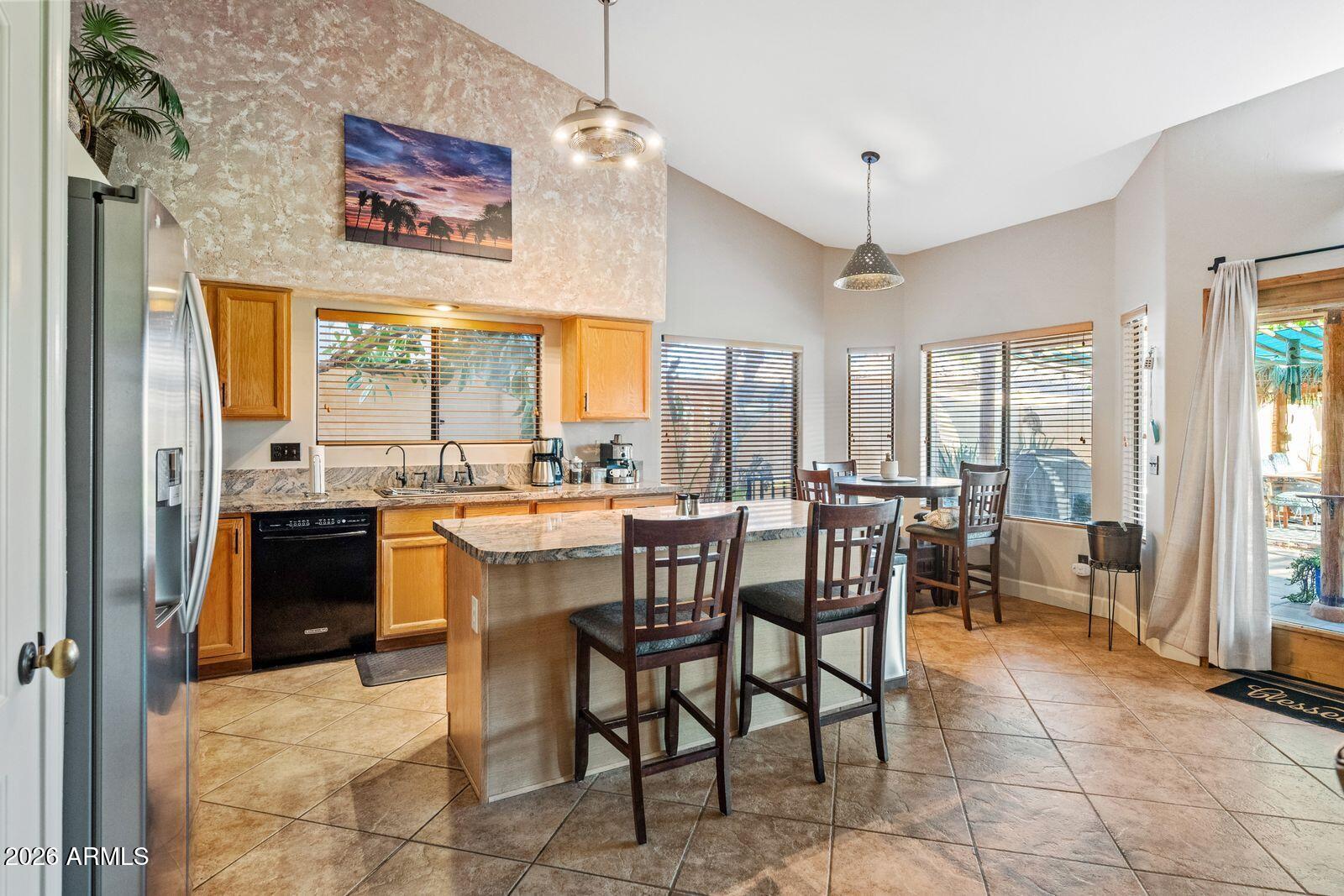 Kitchen and dining area with a granite island, wood cabinetry, and windows overlooking a covered patio.