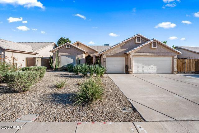 Tan stucco home with a two-car garage, wide driveway, and gravel desert landscaping.