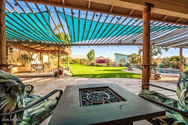 Backyard patio beneath a turquoise-shaded pergola, with a fire table, lawn, and swimming pool.