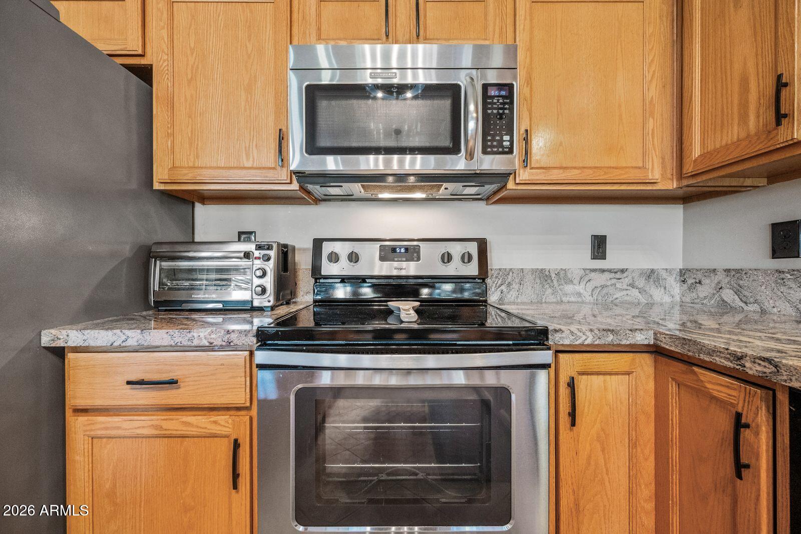 Kitchen with wood cabinets, granite counters, and stainless steel microwave and range.