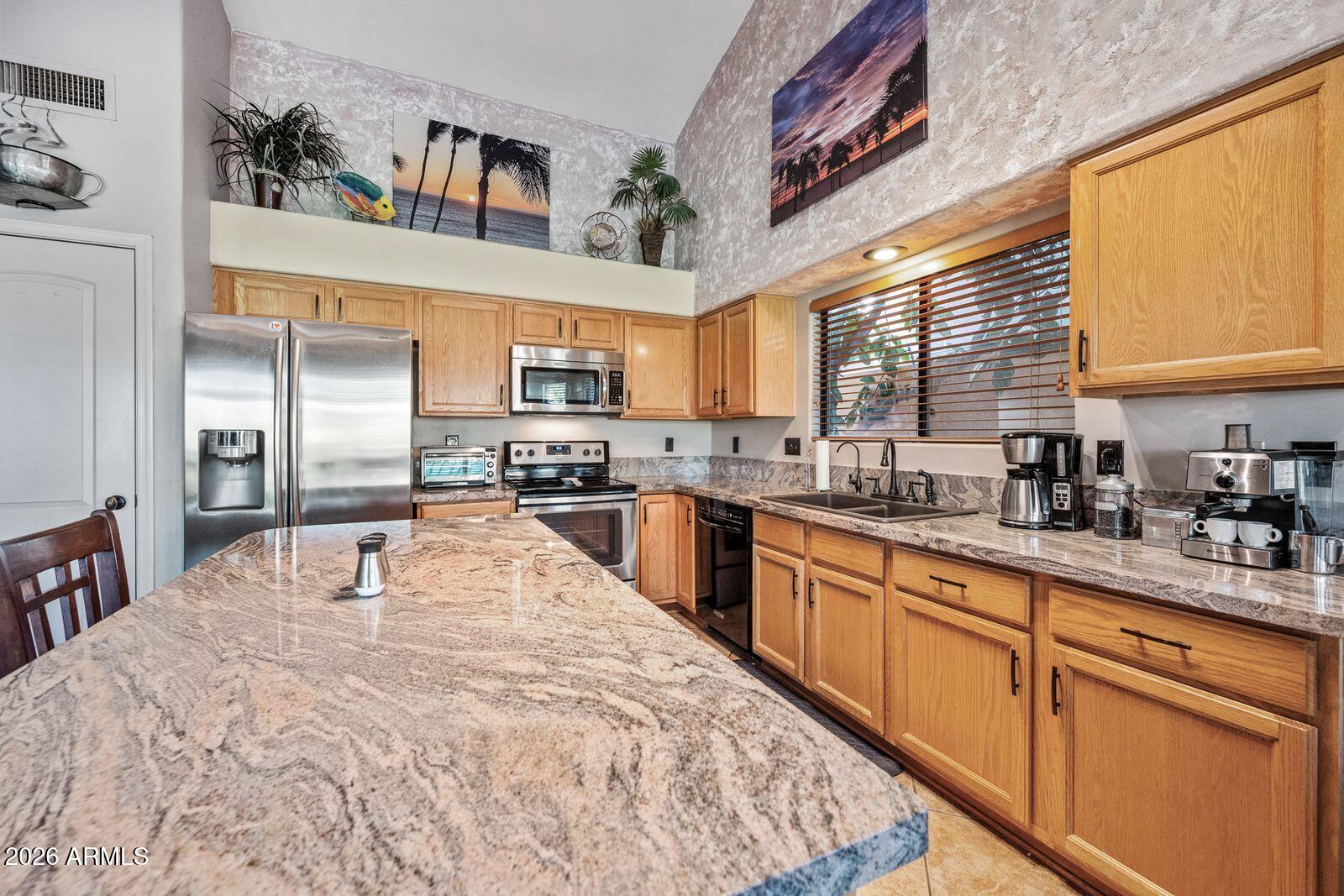 Kitchen with a granite island, honey-colored wood cabinets, stainless steel appliances, and a high vaulted ceiling.