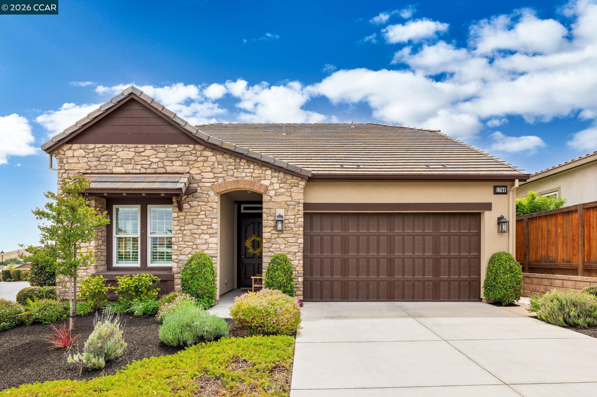 Stone-fronted home with brown garage door, landscaped garden, and driveway.