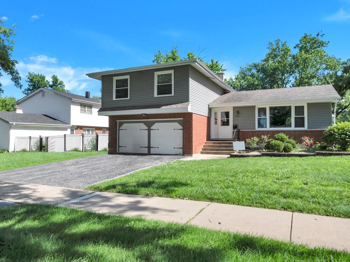 Gray split-level home with a brick facade, double garage, front steps, and a wide lawn.