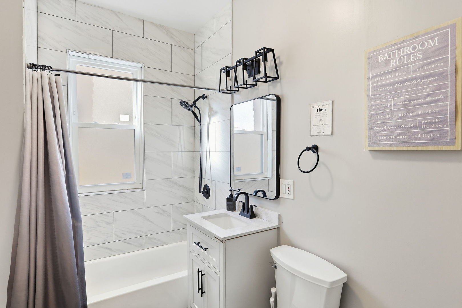 Bathroom with marble-look shower tile, a white vanity, and black fixtures.