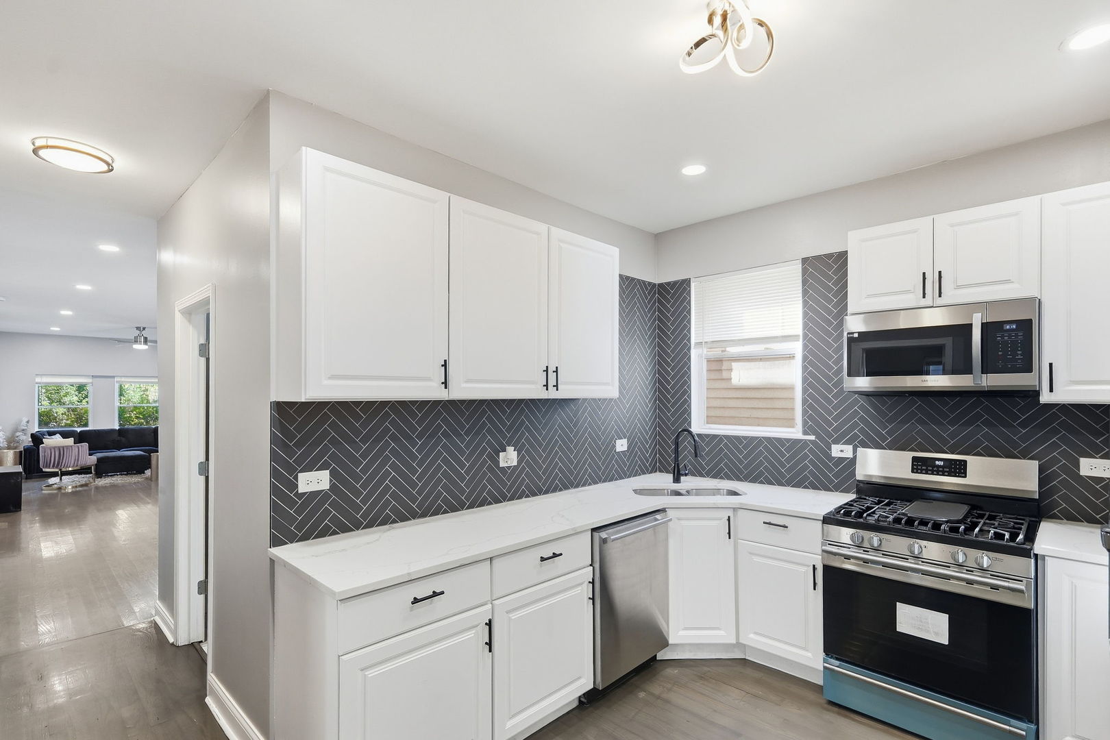 Modern kitchen with dark herringbone backsplash, white cabinets, and stainless steel appliances.