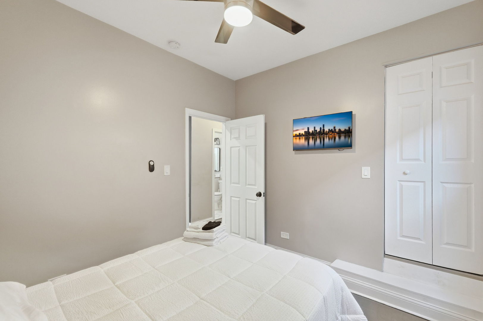 Bedroom with a white quilted bed, ceiling fan, and a closet beside the bathroom doorway.