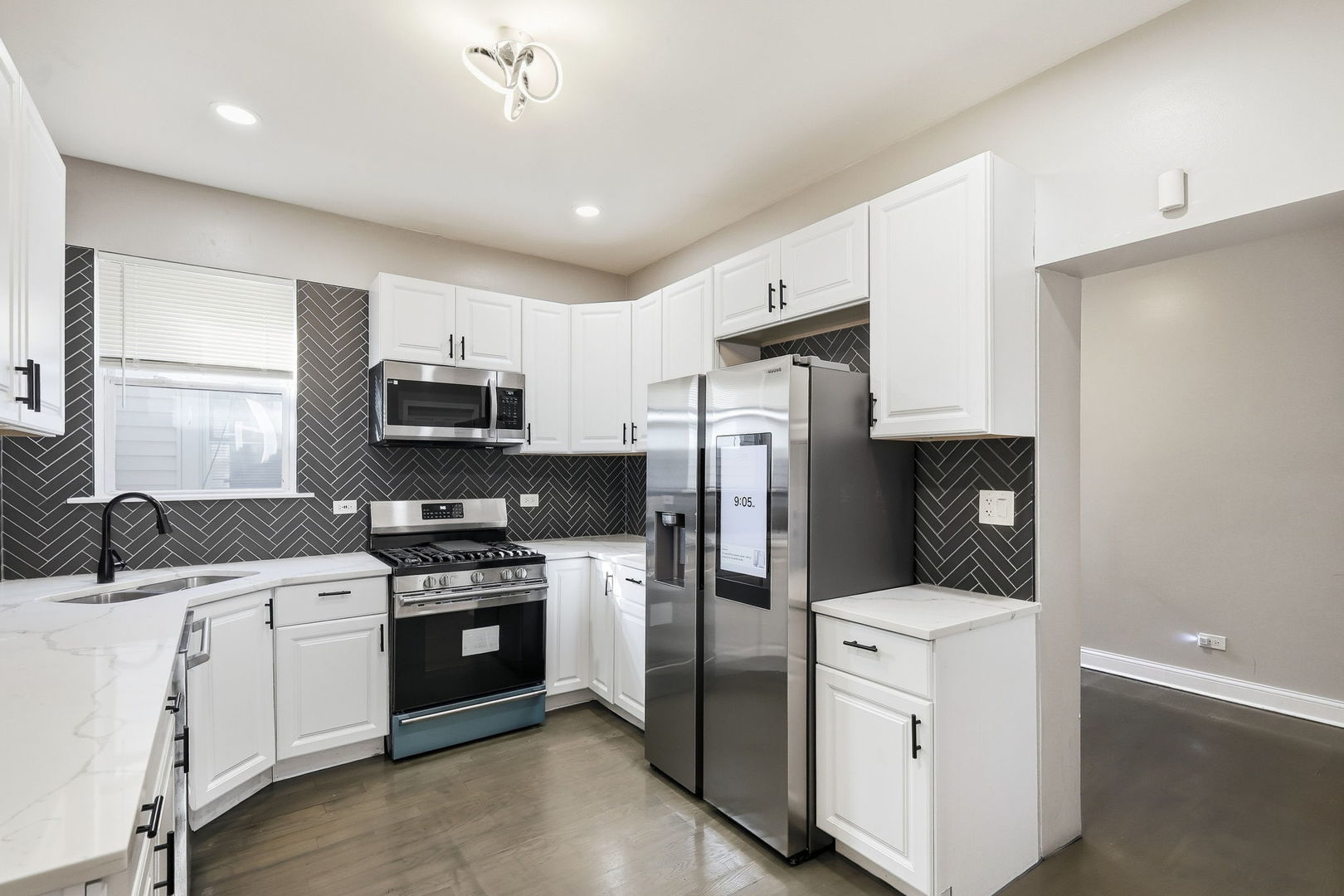 Kitchen with white cabinets, dark herringbone backsplash, and stainless steel appliances.