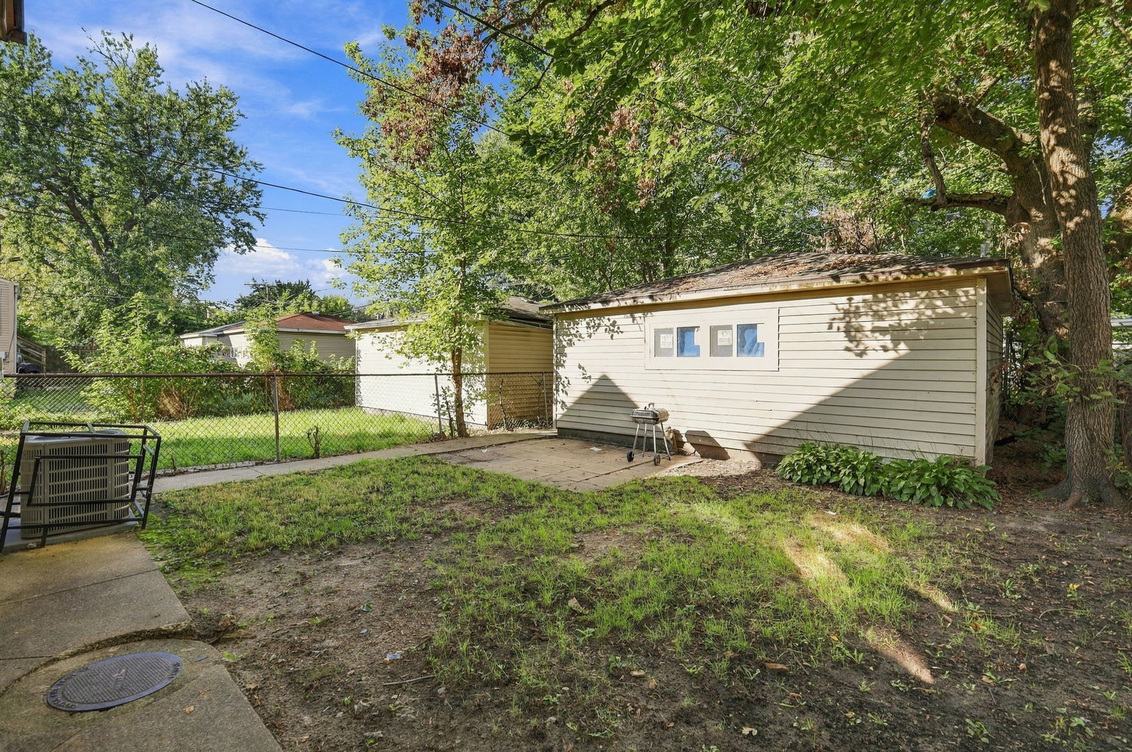 Backyard with a detached shed, fenced lawn, patio, and mature trees.