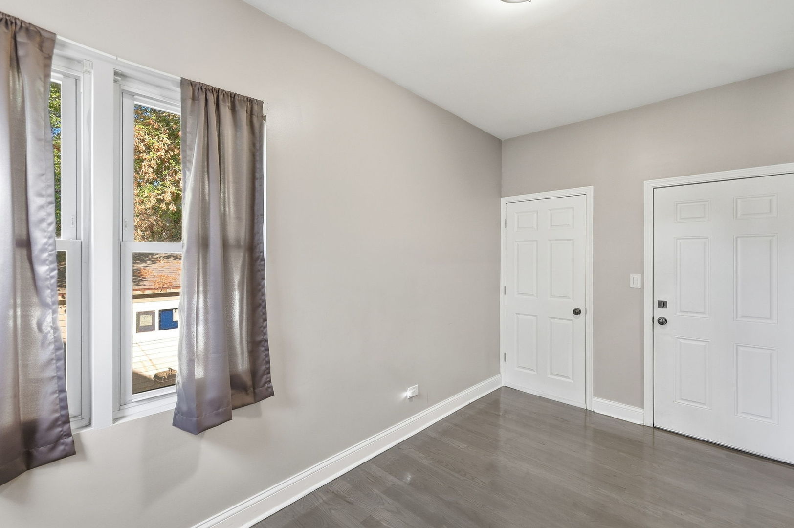 Empty room with gray flooring, curtained windows, and two white doors.